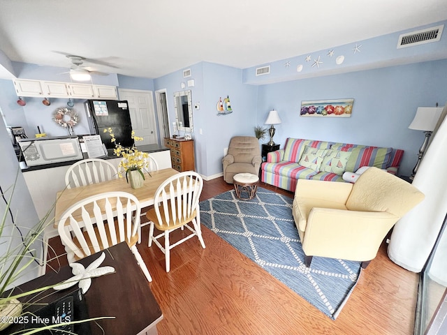 living area with a ceiling fan, visible vents, baseboards, and wood finished floors