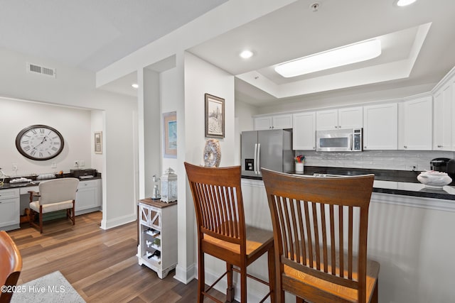 kitchen with a tray ceiling, dark hardwood / wood-style flooring, white cabinets, and appliances with stainless steel finishes