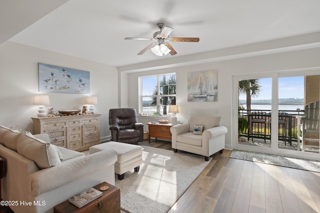 living room with ceiling fan, a water view, and light wood-type flooring