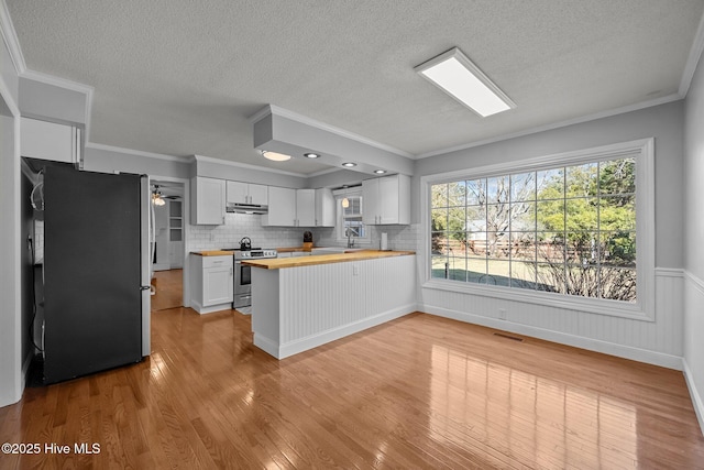 kitchen featuring white cabinetry, wooden counters, stainless steel appliances, ornamental molding, and light hardwood / wood-style flooring