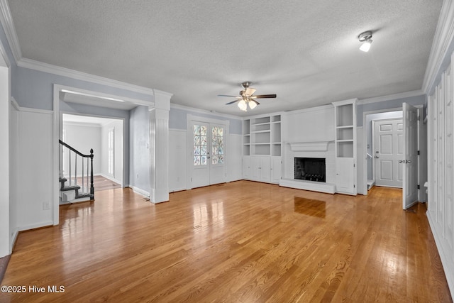 unfurnished living room with ceiling fan, light wood-type flooring, built in features, a fireplace, and a textured ceiling