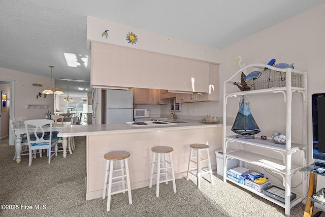 kitchen featuring a kitchen breakfast bar, kitchen peninsula, pendant lighting, light colored carpet, and white appliances