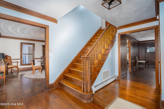 stairway with wooden walls, a baseboard radiator, hardwood / wood-style flooring, and crown molding