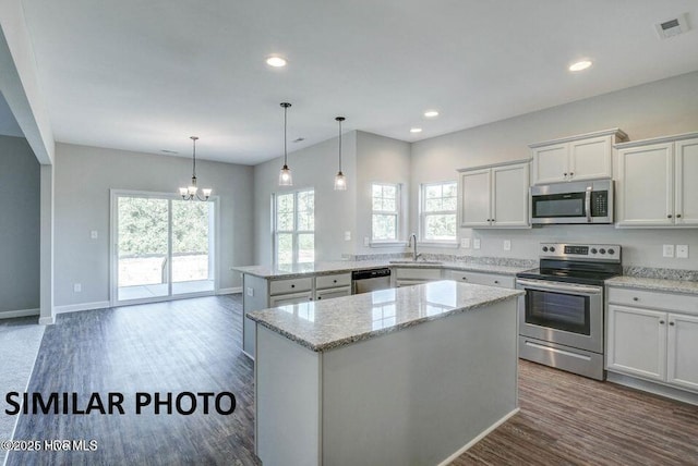 kitchen featuring appliances with stainless steel finishes, white cabinetry, light stone counters, a kitchen island, and kitchen peninsula