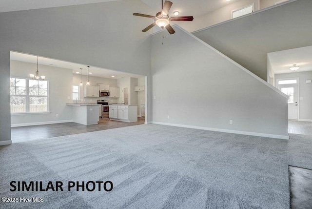 unfurnished living room with ceiling fan with notable chandelier, high vaulted ceiling, and carpet flooring