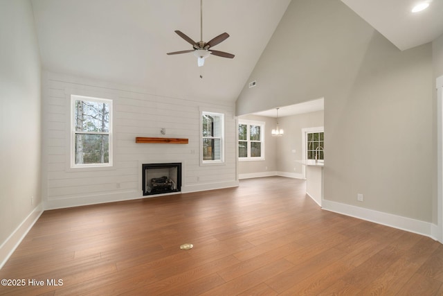 unfurnished living room featuring ceiling fan with notable chandelier, plenty of natural light, and hardwood / wood-style floors