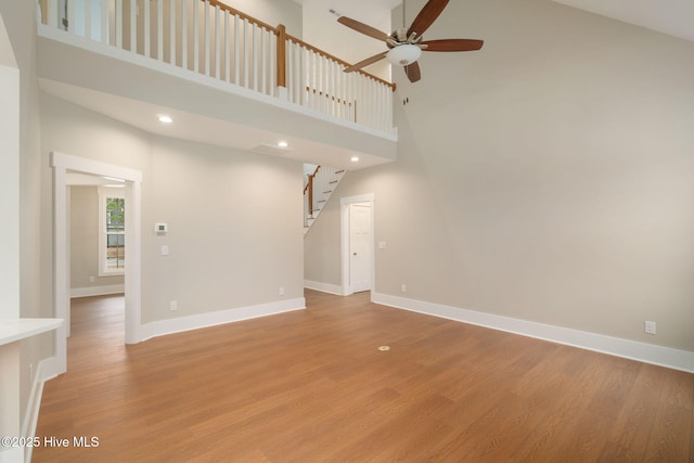 unfurnished living room featuring light hardwood / wood-style floors, ceiling fan, and a high ceiling