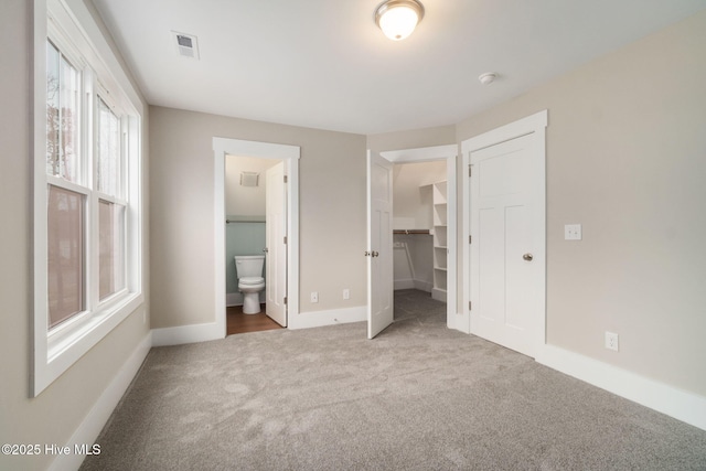 unfurnished bedroom featuring a closet, connected bathroom, a spacious closet, and carpet