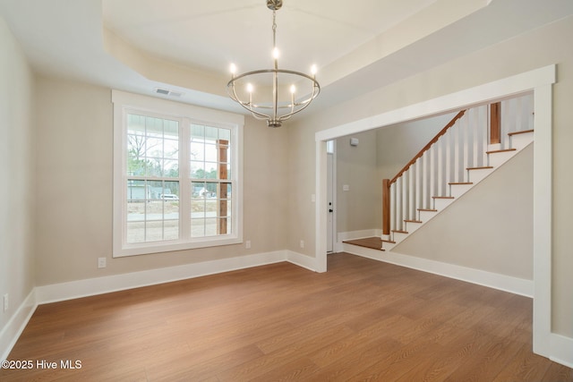 spare room with an inviting chandelier, a raised ceiling, and light wood-type flooring