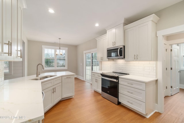 kitchen with sink, appliances with stainless steel finishes, white cabinetry, hanging light fixtures, and light wood-type flooring