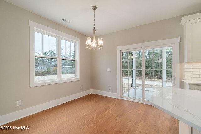 unfurnished dining area with plenty of natural light, light hardwood / wood-style floors, and a notable chandelier