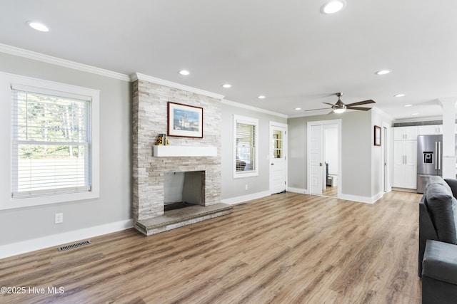 unfurnished living room with light wood-type flooring, a stone fireplace, ceiling fan, and ornamental molding