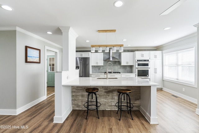 kitchen featuring wall chimney exhaust hood, pendant lighting, a breakfast bar area, white cabinets, and appliances with stainless steel finishes