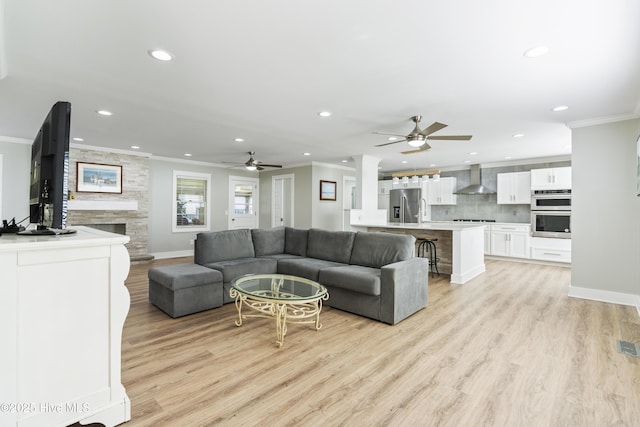 living room with light hardwood / wood-style flooring, ceiling fan, crown molding, and a stone fireplace