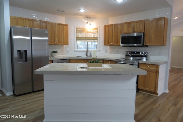 kitchen with sink, light hardwood / wood-style flooring, decorative backsplash, appliances with stainless steel finishes, and a kitchen island