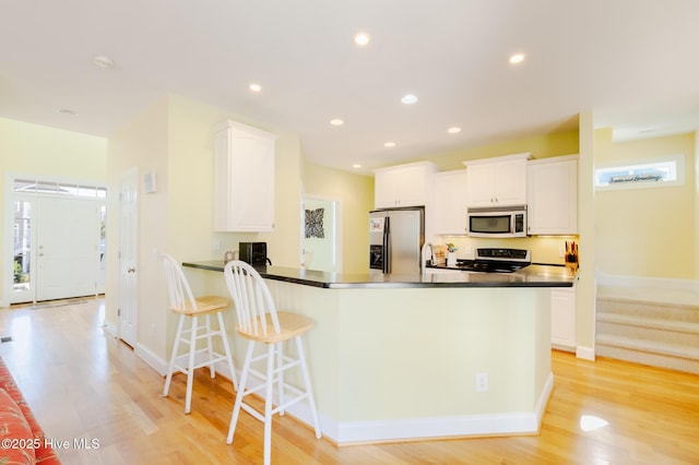 kitchen with kitchen peninsula, stainless steel fridge, stove, white cabinets, and light hardwood / wood-style floors