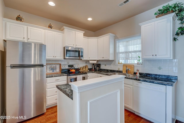 kitchen with appliances with stainless steel finishes, tasteful backsplash, sink, white cabinets, and a kitchen island