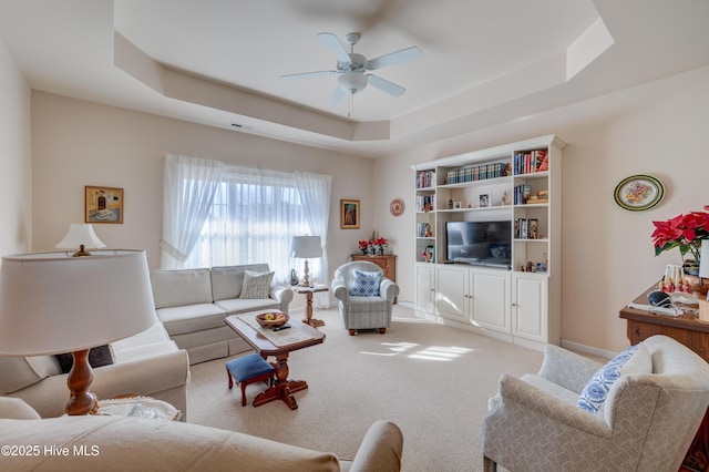 living room with ceiling fan, a raised ceiling, and light carpet