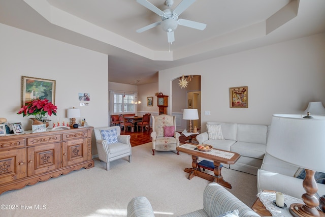 living room featuring a raised ceiling, ceiling fan, and carpet