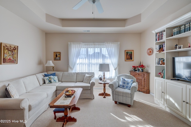 living room with a raised ceiling, ceiling fan, and carpet