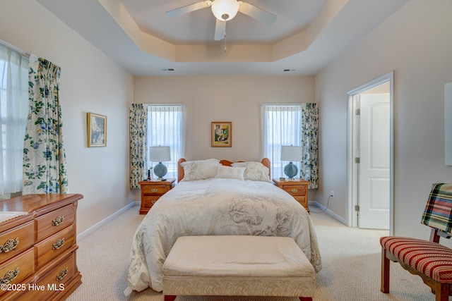 bedroom featuring ceiling fan, multiple windows, light carpet, and a tray ceiling