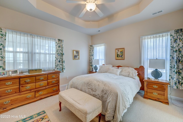 bedroom featuring ceiling fan, light colored carpet, and a tray ceiling