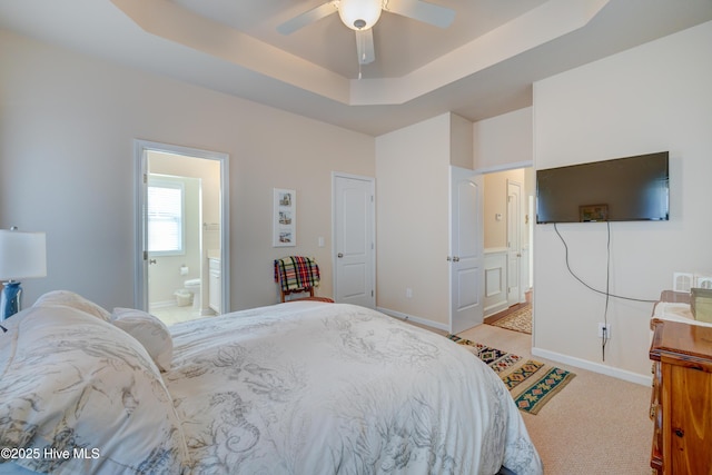 bedroom featuring a raised ceiling, ensuite bath, ceiling fan, and light carpet