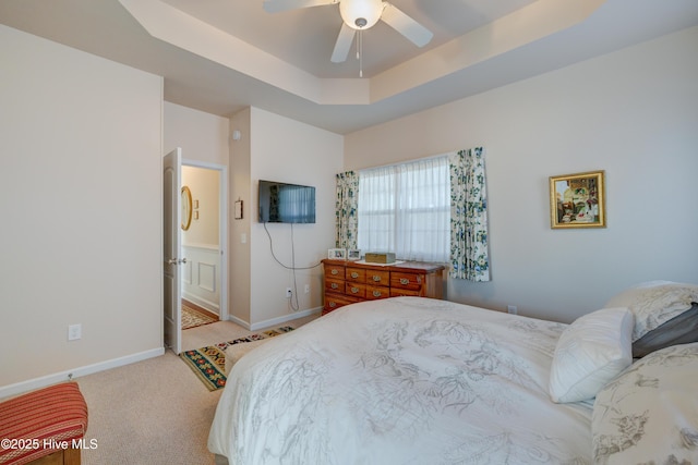 bedroom with light carpet, connected bathroom, a raised ceiling, and ceiling fan