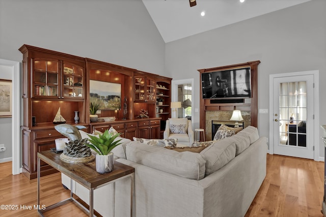 living room featuring a high end fireplace, light hardwood / wood-style floors, high vaulted ceiling, and ceiling fan