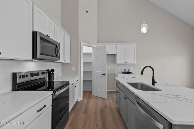 kitchen with high vaulted ceiling, hanging light fixtures, sink, appliances with stainless steel finishes, and white cabinetry