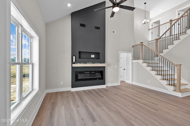 unfurnished living room featuring hardwood / wood-style floors, ceiling fan with notable chandelier, a large fireplace, and high vaulted ceiling