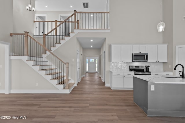 kitchen featuring white cabinetry, sink, hanging light fixtures, stainless steel appliances, and a high ceiling