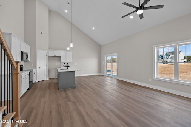 kitchen featuring pendant lighting, black electric range oven, a kitchen island with sink, and high vaulted ceiling