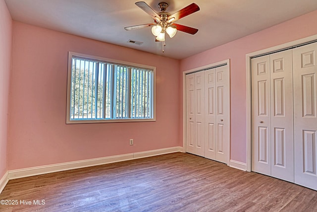 unfurnished bedroom with multiple closets, ceiling fan, and wood-type flooring