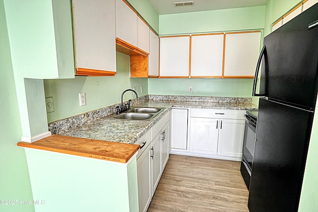 kitchen with light wood-type flooring, white cabinetry, sink, and black appliances