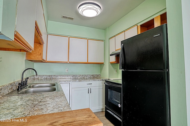 kitchen featuring white cabinets, black refrigerator, range, and sink