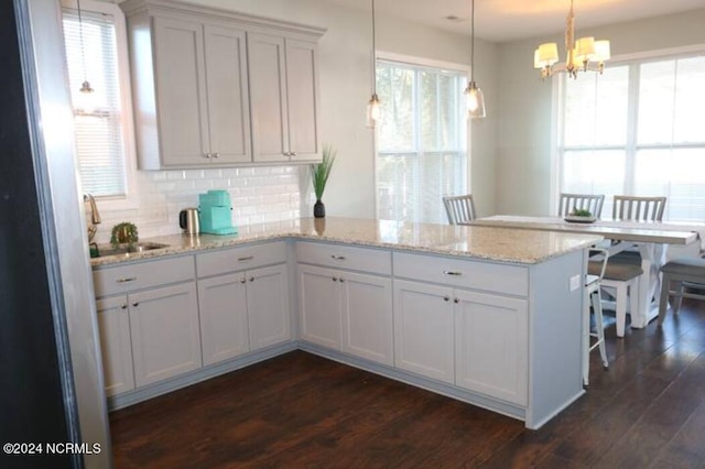 kitchen with white cabinetry, dark wood-type flooring, hanging light fixtures, tasteful backsplash, and kitchen peninsula