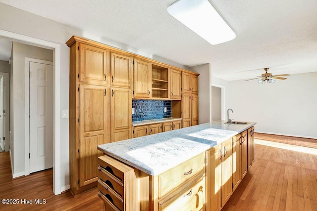 kitchen featuring backsplash, a kitchen island with sink, sink, ceiling fan, and wood-type flooring