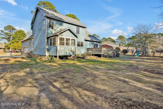 rear view of property featuring a playground, a deck, and a garage