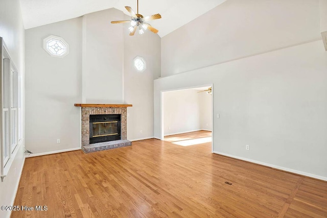 unfurnished living room with high vaulted ceiling, a brick fireplace, ceiling fan, and light hardwood / wood-style floors