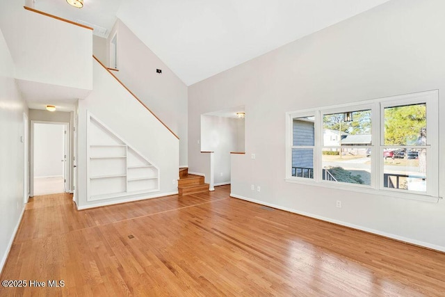 unfurnished living room with built in shelves, high vaulted ceiling, and light hardwood / wood-style floors