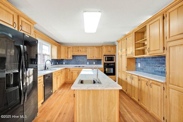 kitchen with black appliances, sink, an island with sink, and tasteful backsplash