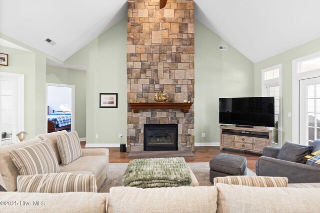 living room with ceiling fan with notable chandelier, a stone fireplace, light wood-type flooring, and high vaulted ceiling