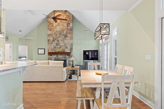 4379 Gauntlet Dr, Southport, NC 28461 - dining area featuring wood finished floors, a stone fireplace, a ceiling fan, high vaulted ceiling, and baseboards