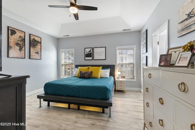 bedroom with multiple windows, light hardwood / wood-style floors, and a raised ceiling