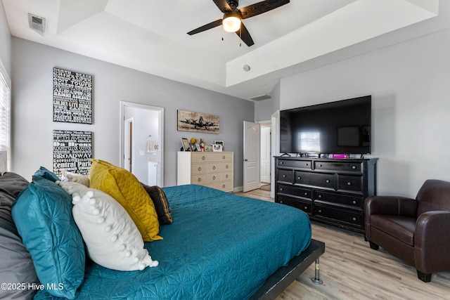 bedroom with wood-type flooring, ensuite bathroom, ceiling fan, and a tray ceiling