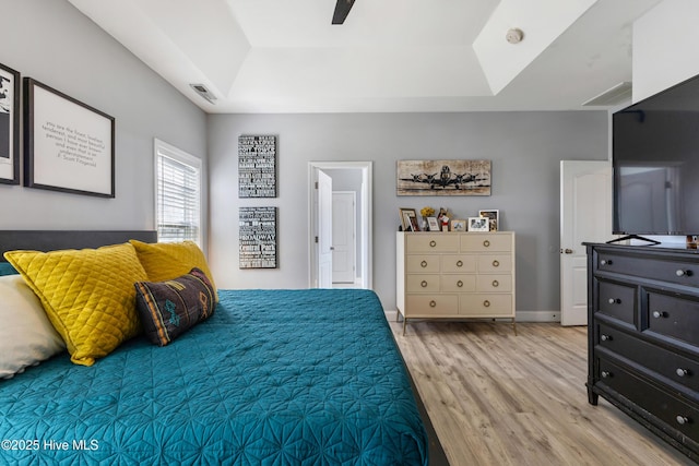 bedroom with ceiling fan, light wood-type flooring, and a tray ceiling