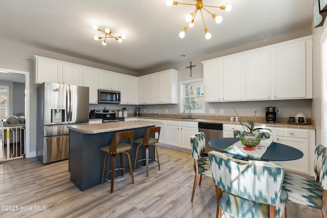 kitchen with sink, a kitchen island, a notable chandelier, stainless steel appliances, and white cabinets