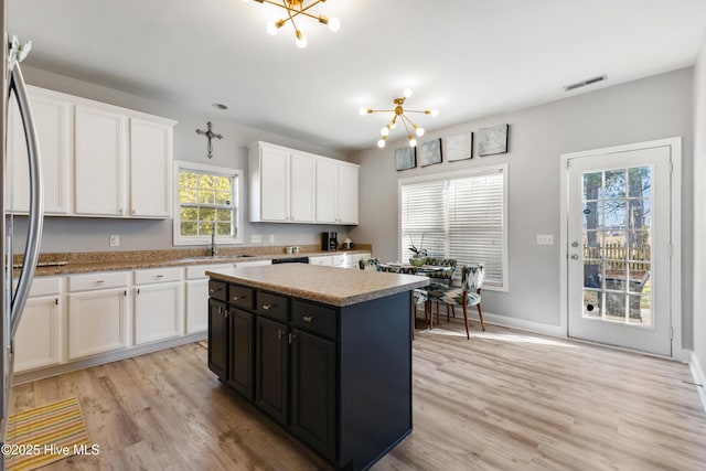 kitchen featuring sink, an inviting chandelier, white cabinetry, stainless steel fridge, and a kitchen island