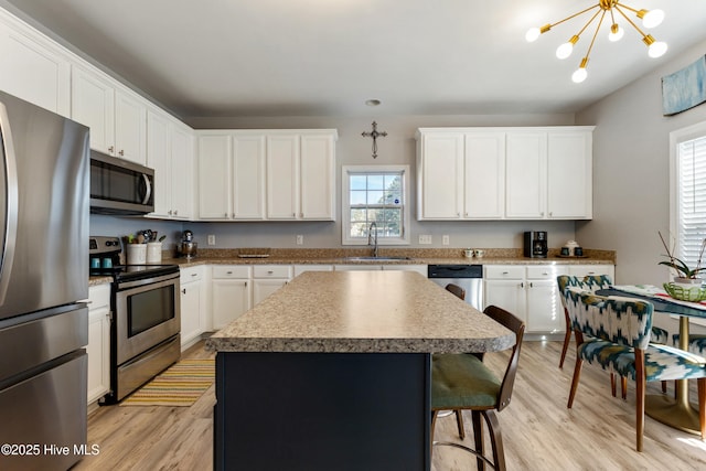 kitchen featuring a kitchen island, sink, white cabinets, stainless steel appliances, and light wood-type flooring